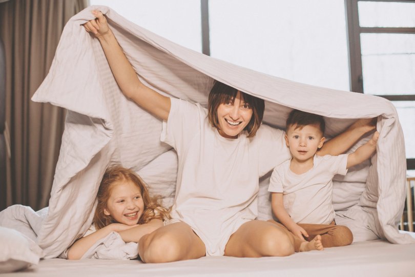 Mère avec son fils et sa fille assis sur un lit sous une couverture